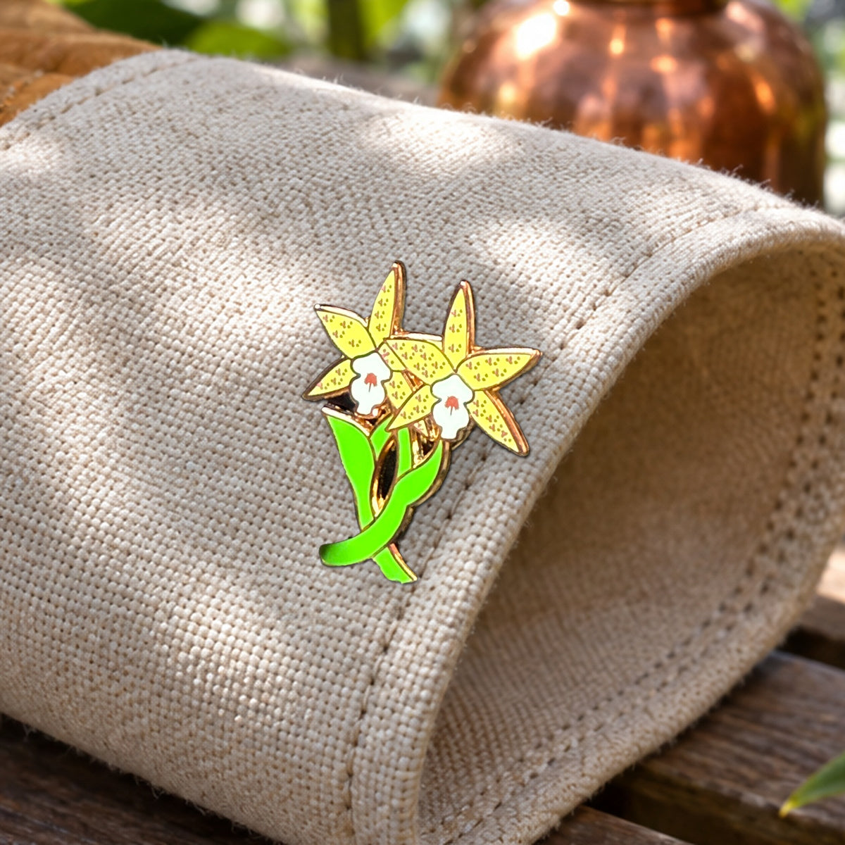 Close-up of the yellow Double Laelia Cattleya orchid enamel pin on a canvas glove cuff