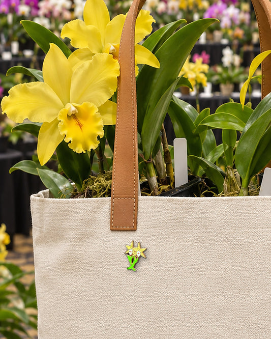 Yellow Double Laelia Cattleya orchid enamel pin on a canvas tote filled with yellow Cattleya orchids at an orchid show