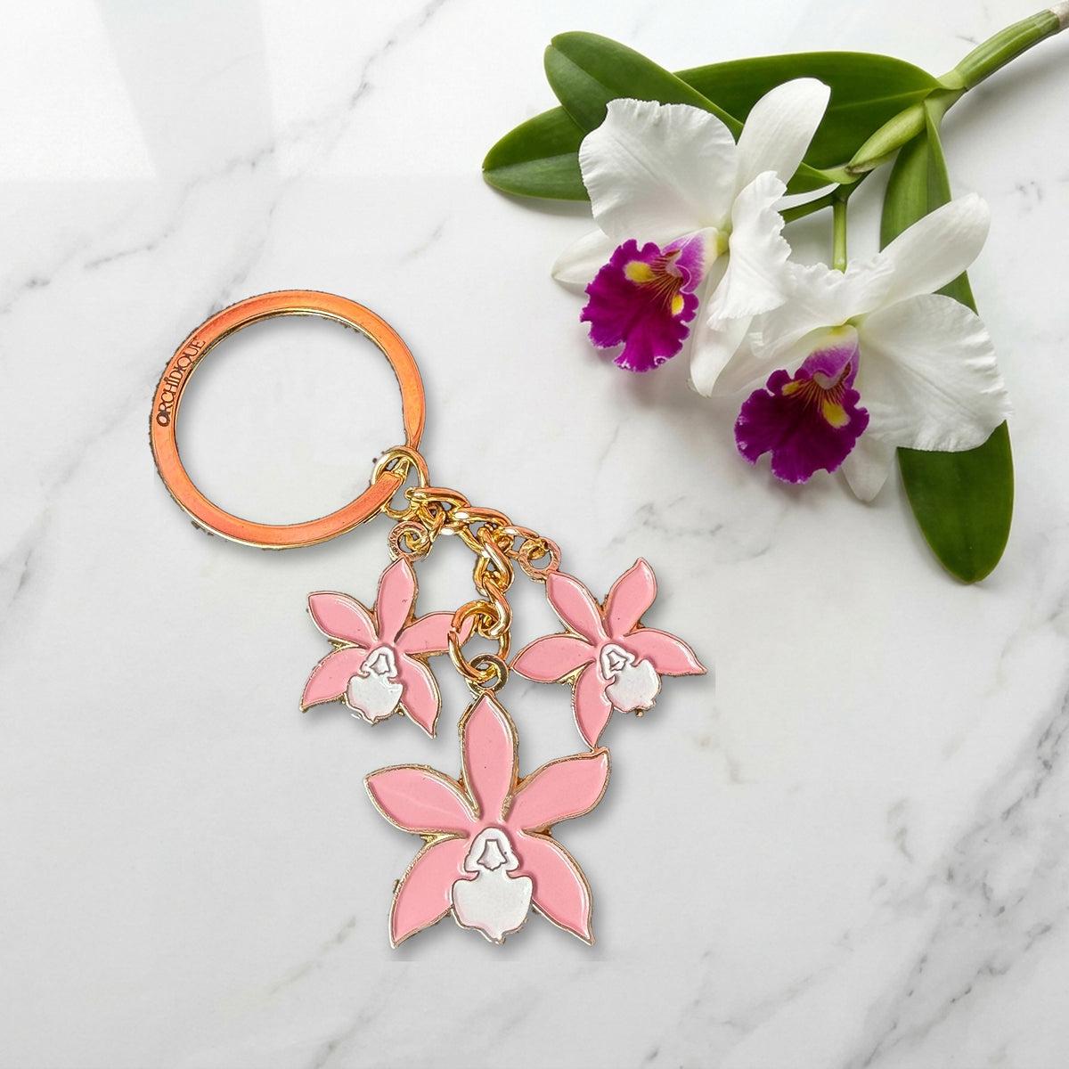 Pink enamel Cattleya orchid keychain on white marble