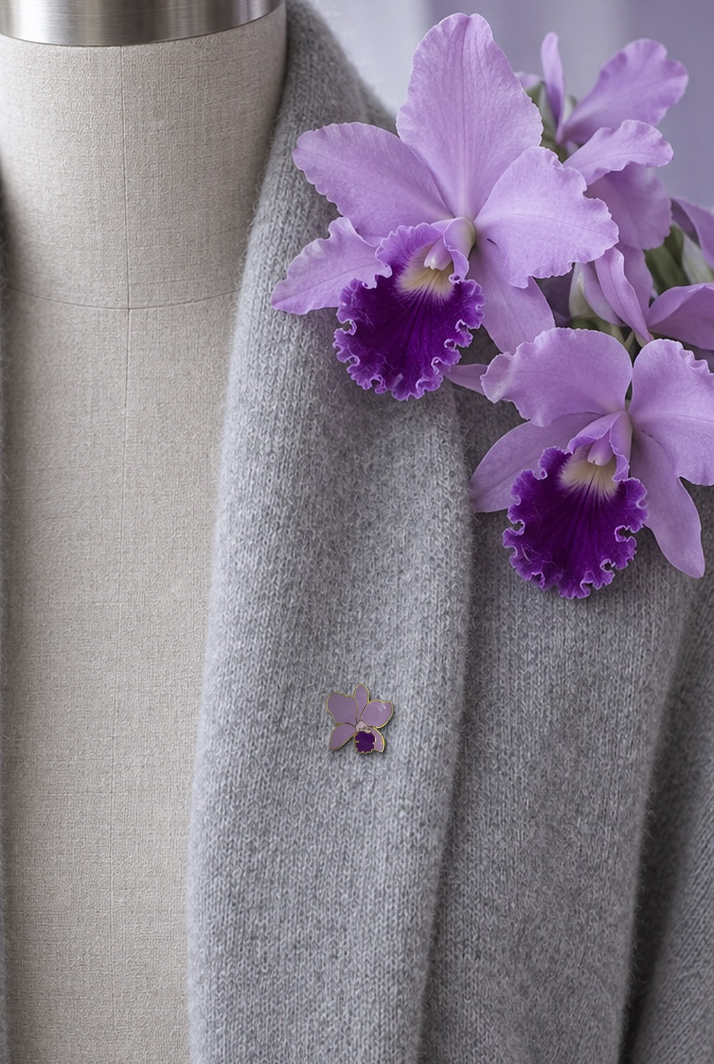 Lavender Lueddemannia orchid enamel pin on a grey cashmere shawl cardigan with lavender Cattleya blooms