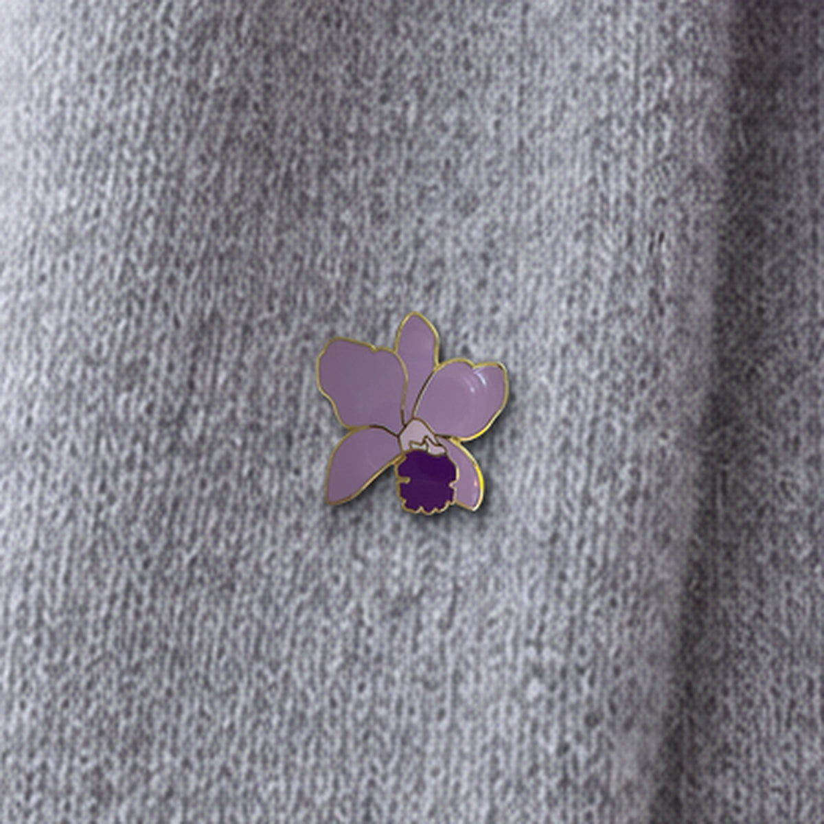 Lavender Lueddemannia enamel pin close-up on grey cashmere