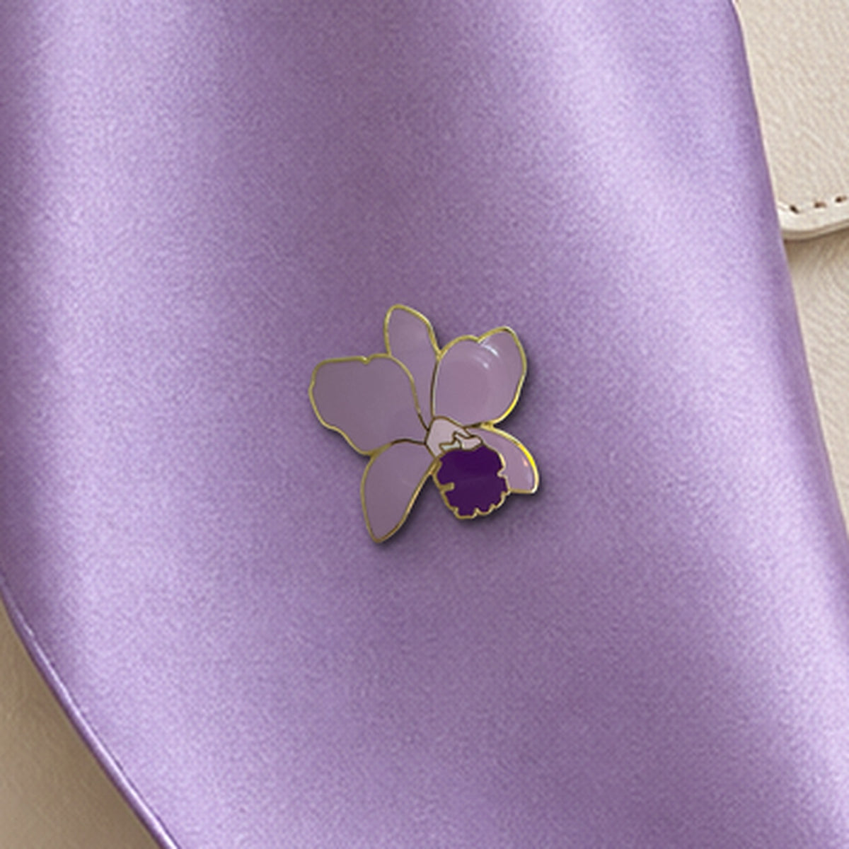 Lavender Lueddemannia enamel pin close-up on a lilac silk scarf