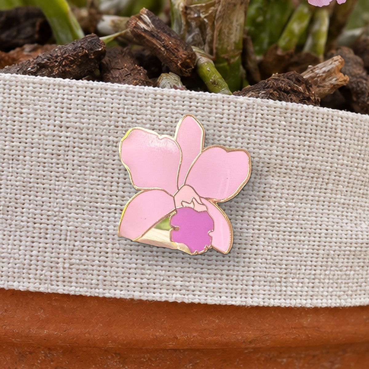 Close-up of the light pink Lueddemannia orchid enamel pin on a natural linen ribbon
