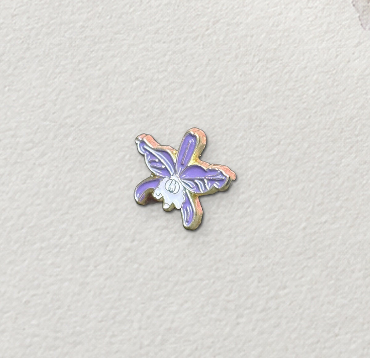 Close-up of the Purple mini Cattleya jenmanii enamel pin with gold-tone outline on watercolor paper