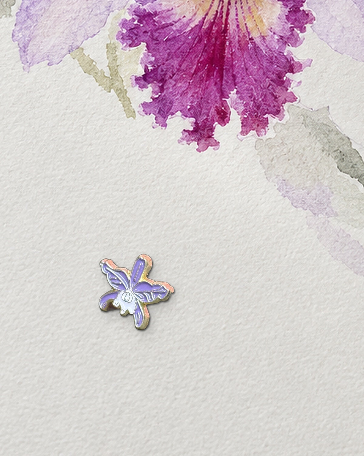 Purple mini Cattleya jenmanii enamel pin on a watercolor sketchbook page below a Cattleya painting in progress