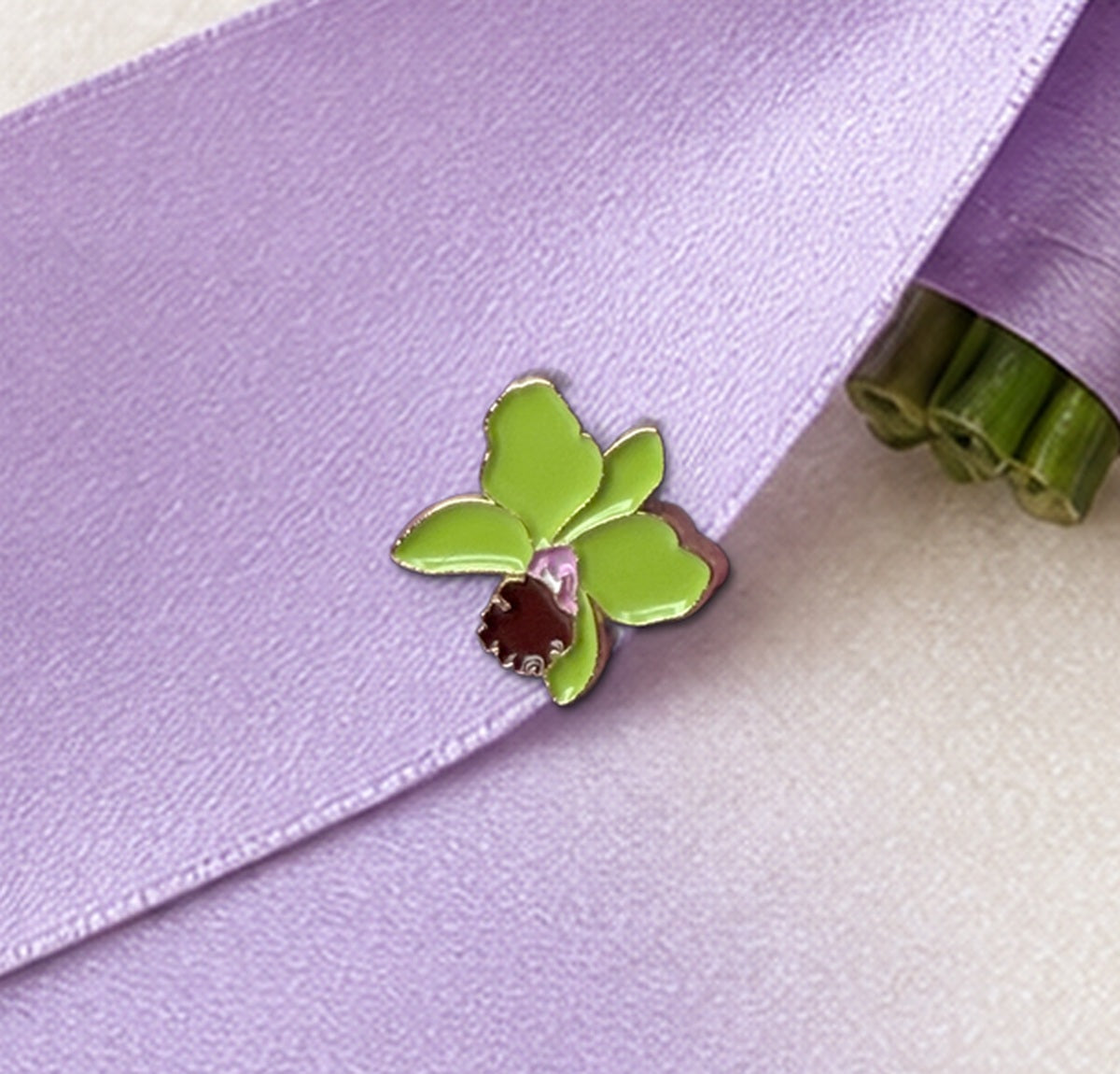 Close-up of the Green mini Cattleya enamel pin with gold-tone outline on lavender satin ribbon