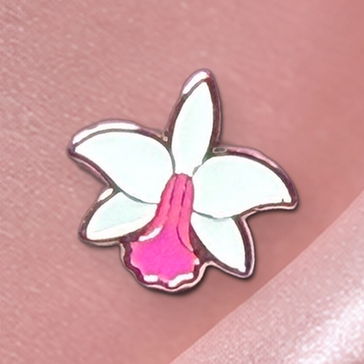 Close-up of the White Pink mini Cattleya violacea enamel pin with gold-tone outline on blush silk