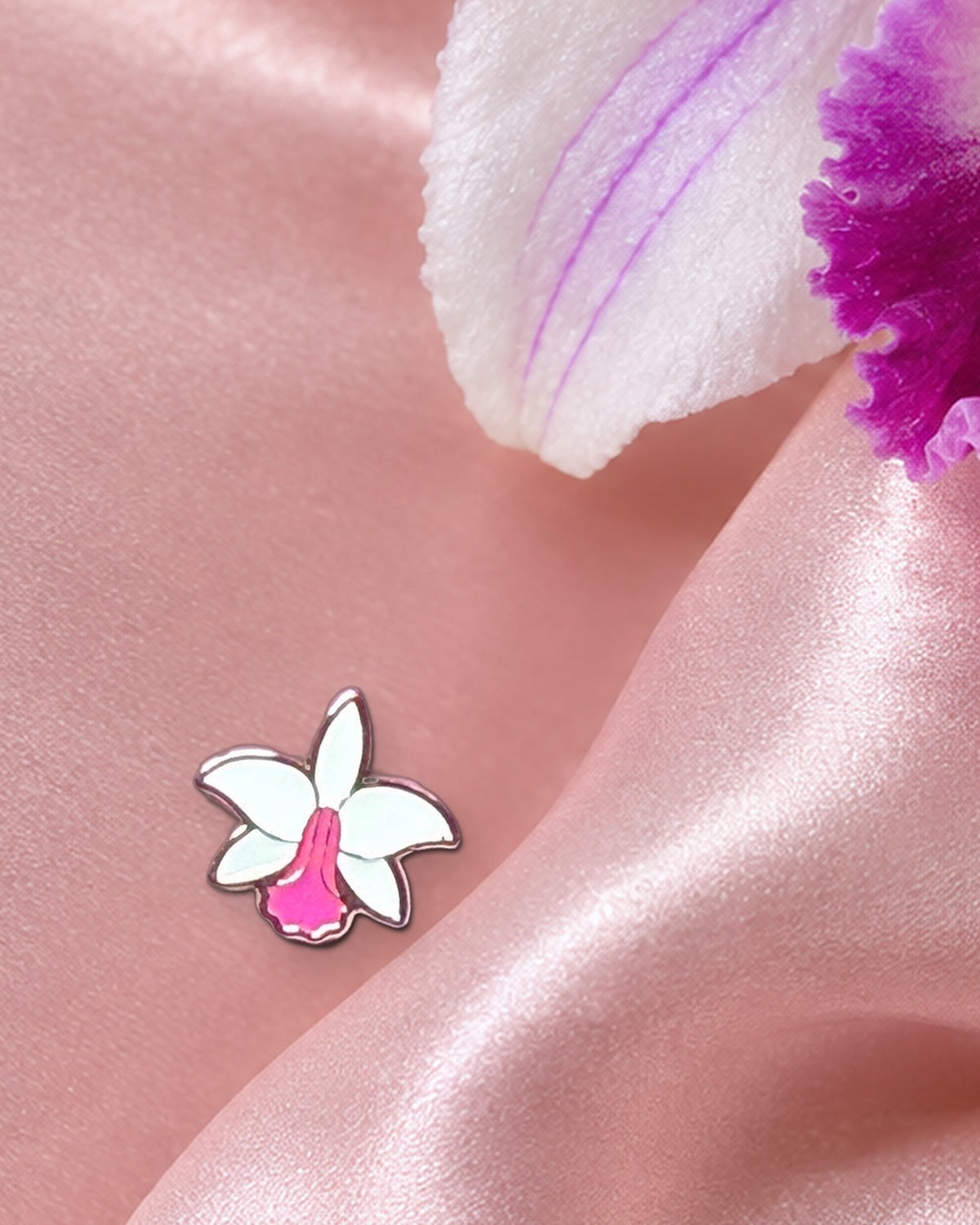 White Pink mini Cattleya violacea enamel pin on blush silk beneath a real violacea orchid bloom