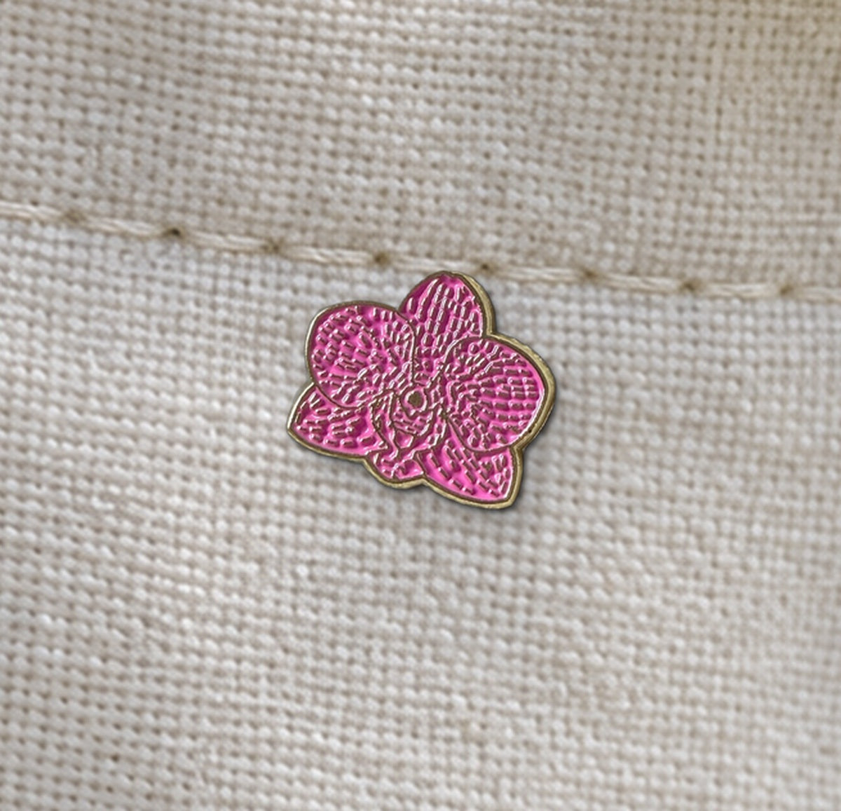 Close-up of the Fuchsia mini Phalaenopsis enamel pin with textured petals and gold-tone outline on linen