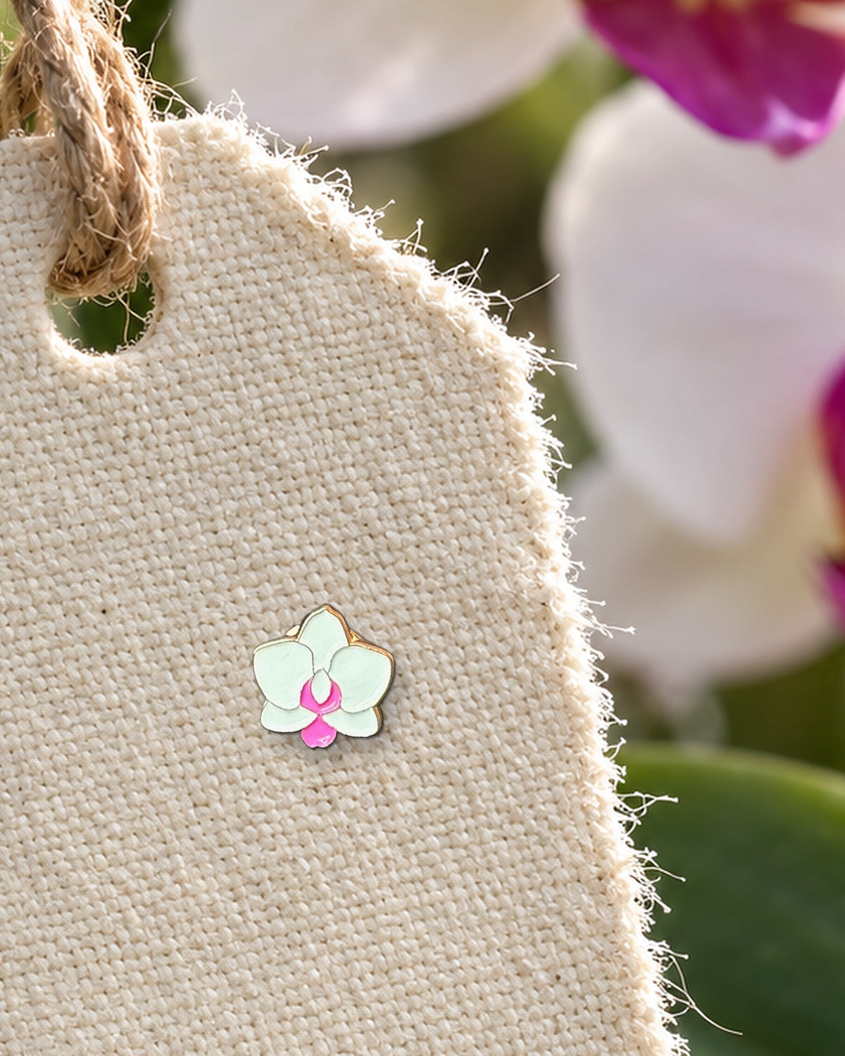 White and pink mini Phalaenopsis orchid enamel pin on a canvas orchid show tag hanging from a Phalaenopsis spike