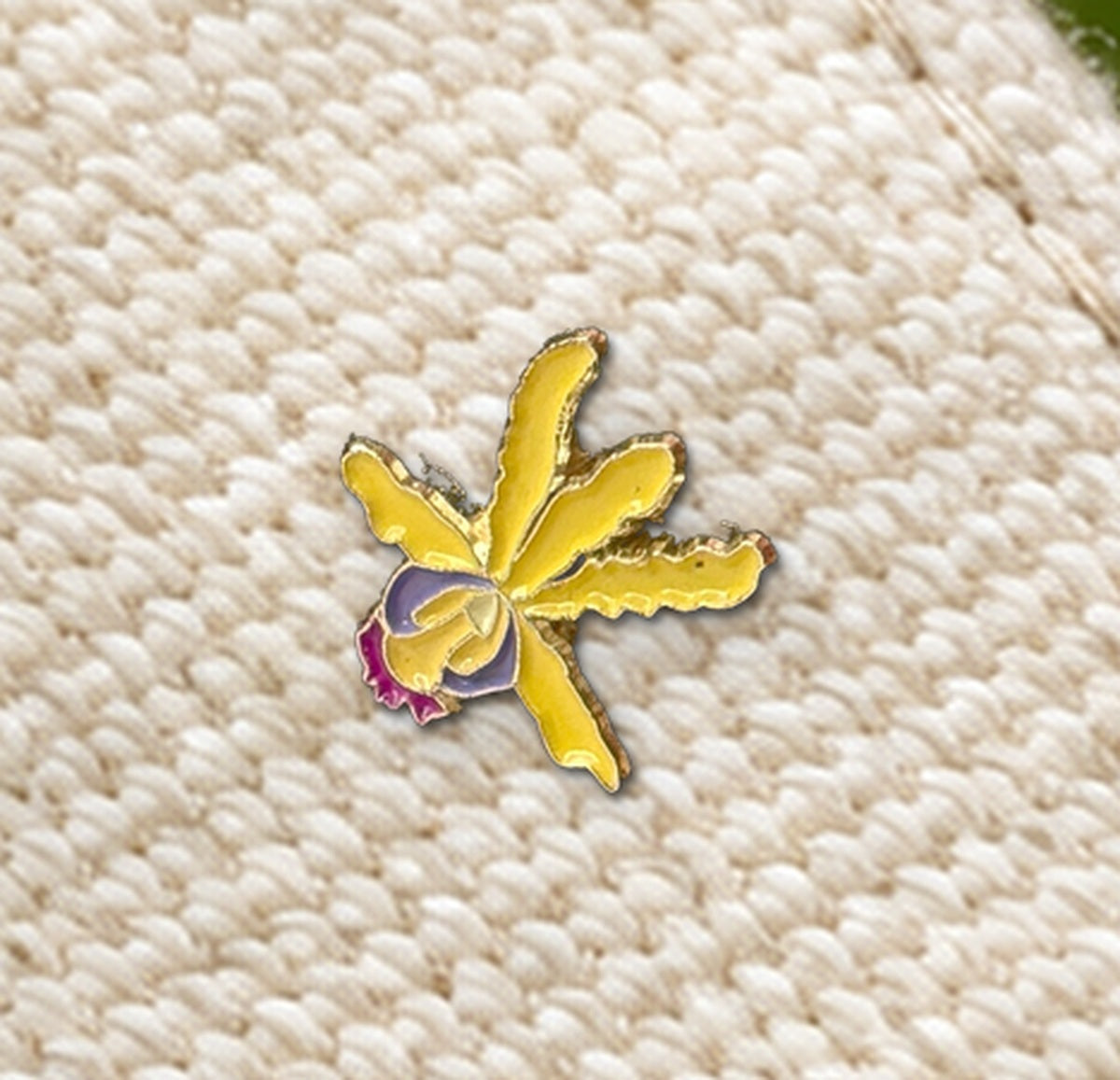Close-up of the Yellow mini Schomburgkia enamel pin with wavy petals and gold-tone outline on woven canvas