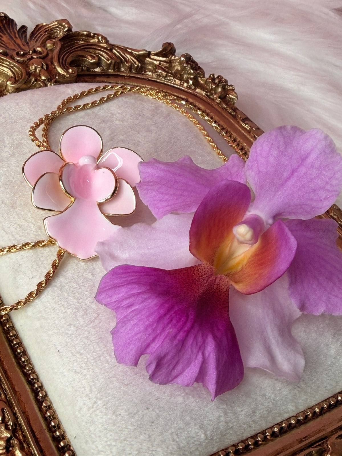Pink enamel Miss Joaquim orchid lariat necklace with gold rope chain beside a real Vanda Miss Joaquim bloom in a gold frame