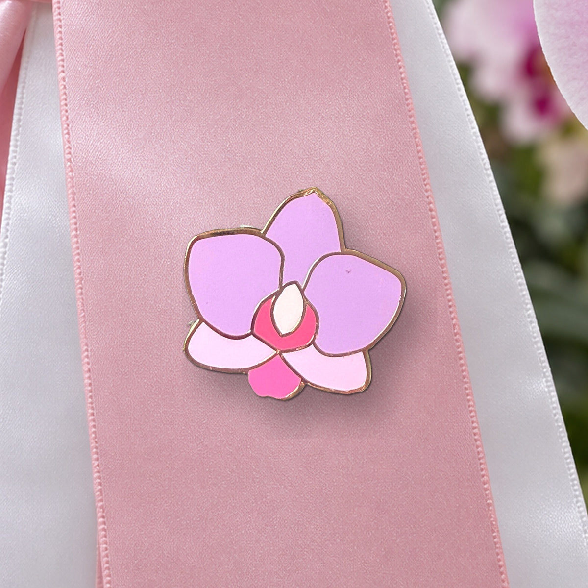 Close-up of the pink Phal Cutie orchid enamel pin on a satin award ribbon