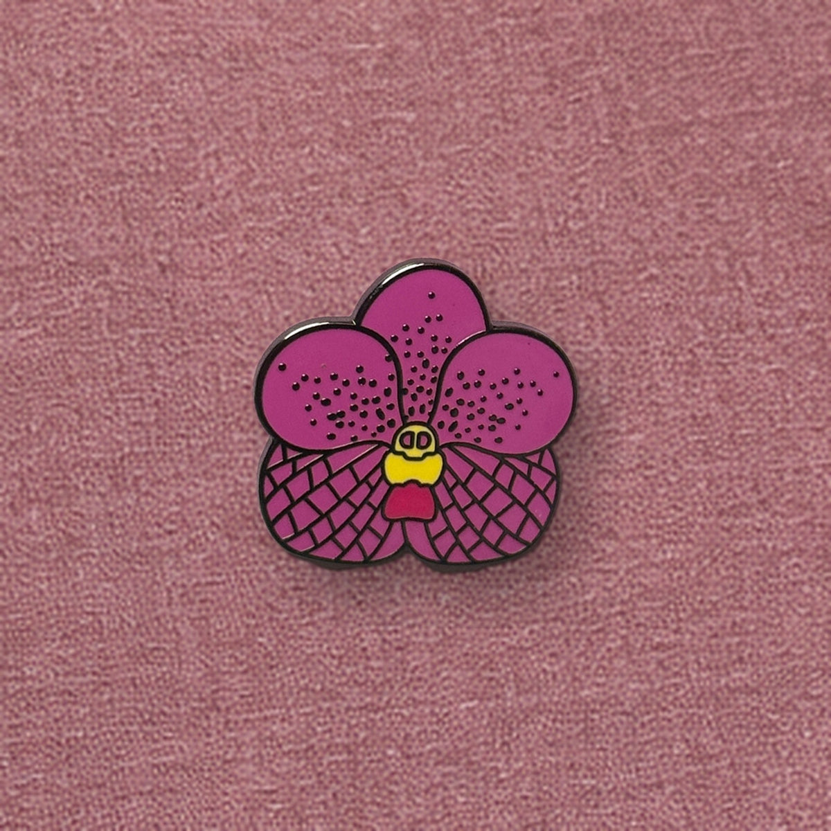 Pink Vanda enamel pin close-up on a linen journal cover