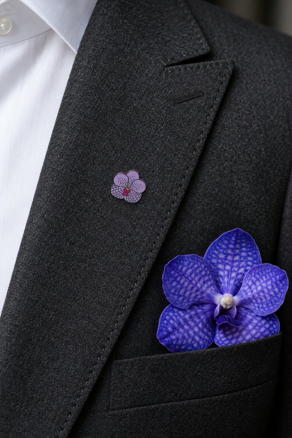 Purple Vanda orchid hard enamel pin worn on a charcoal suit lapel with a real violet Vanda bloom