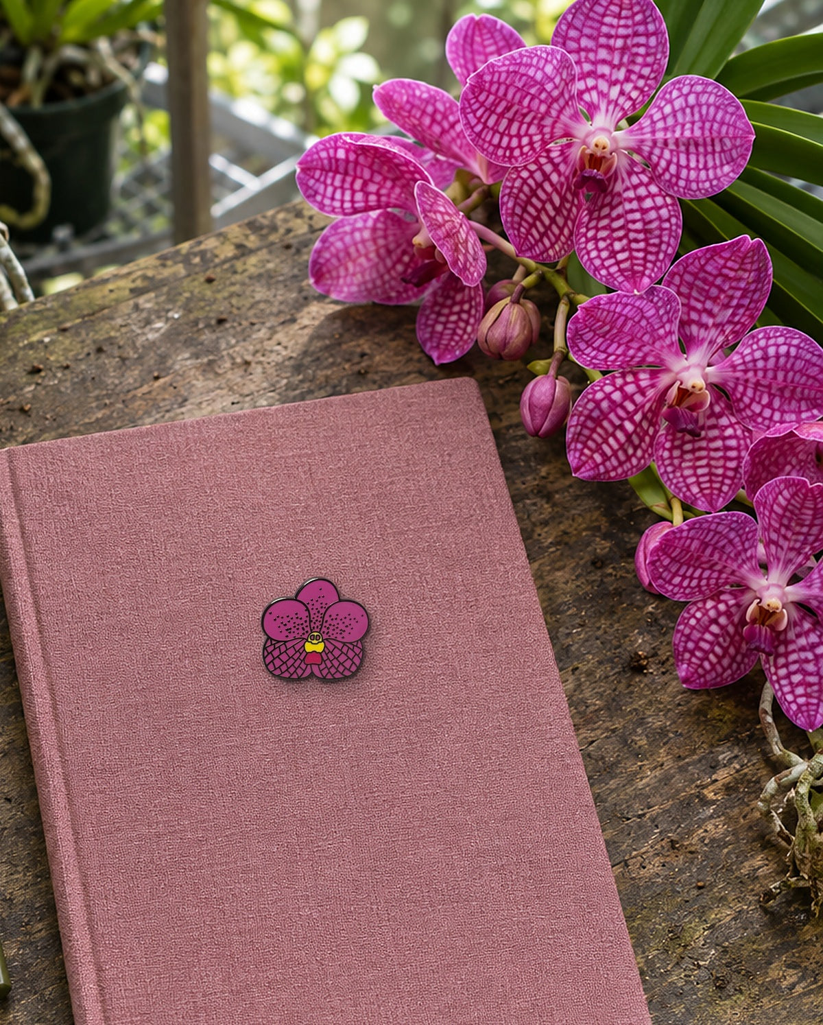 Pink Vanda orchid enamel pin on a linen orchid grow journal beside magenta Vanda blooms